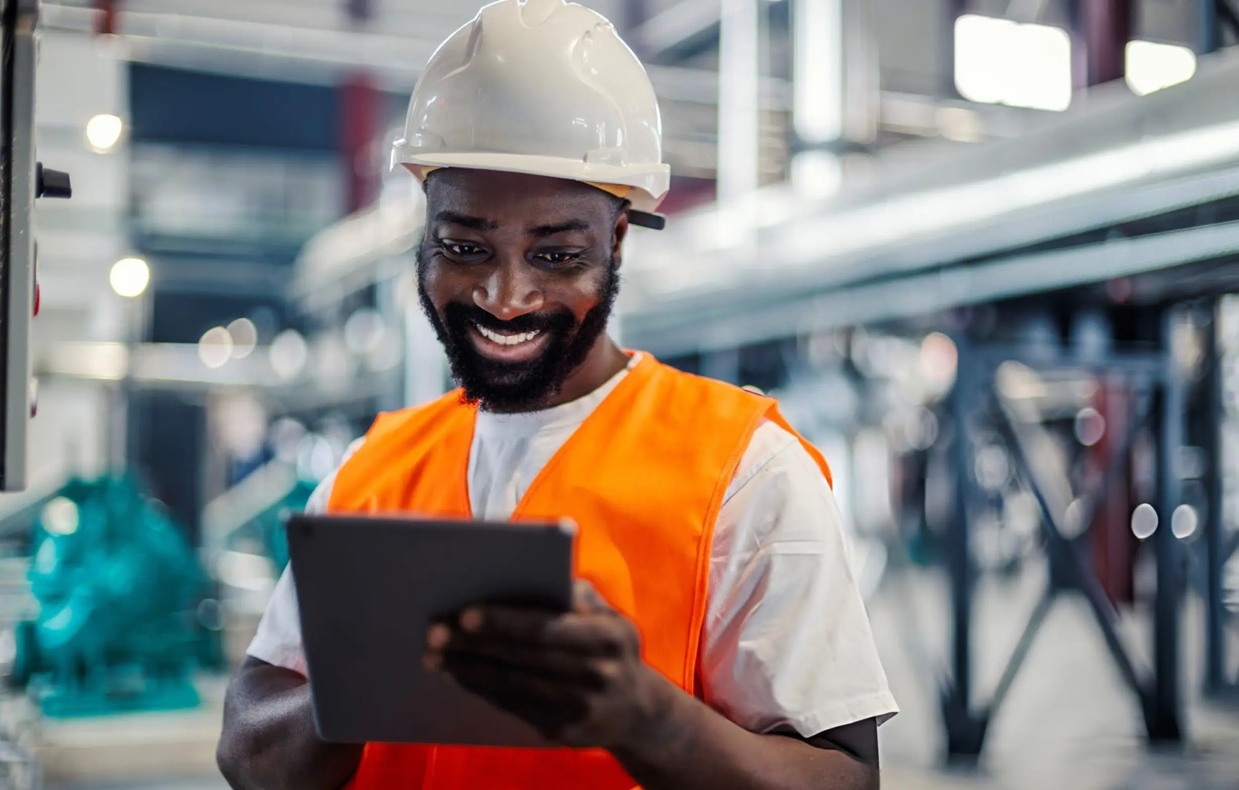 An engineer in a hard hat checks a system on a tablet on the factory floor