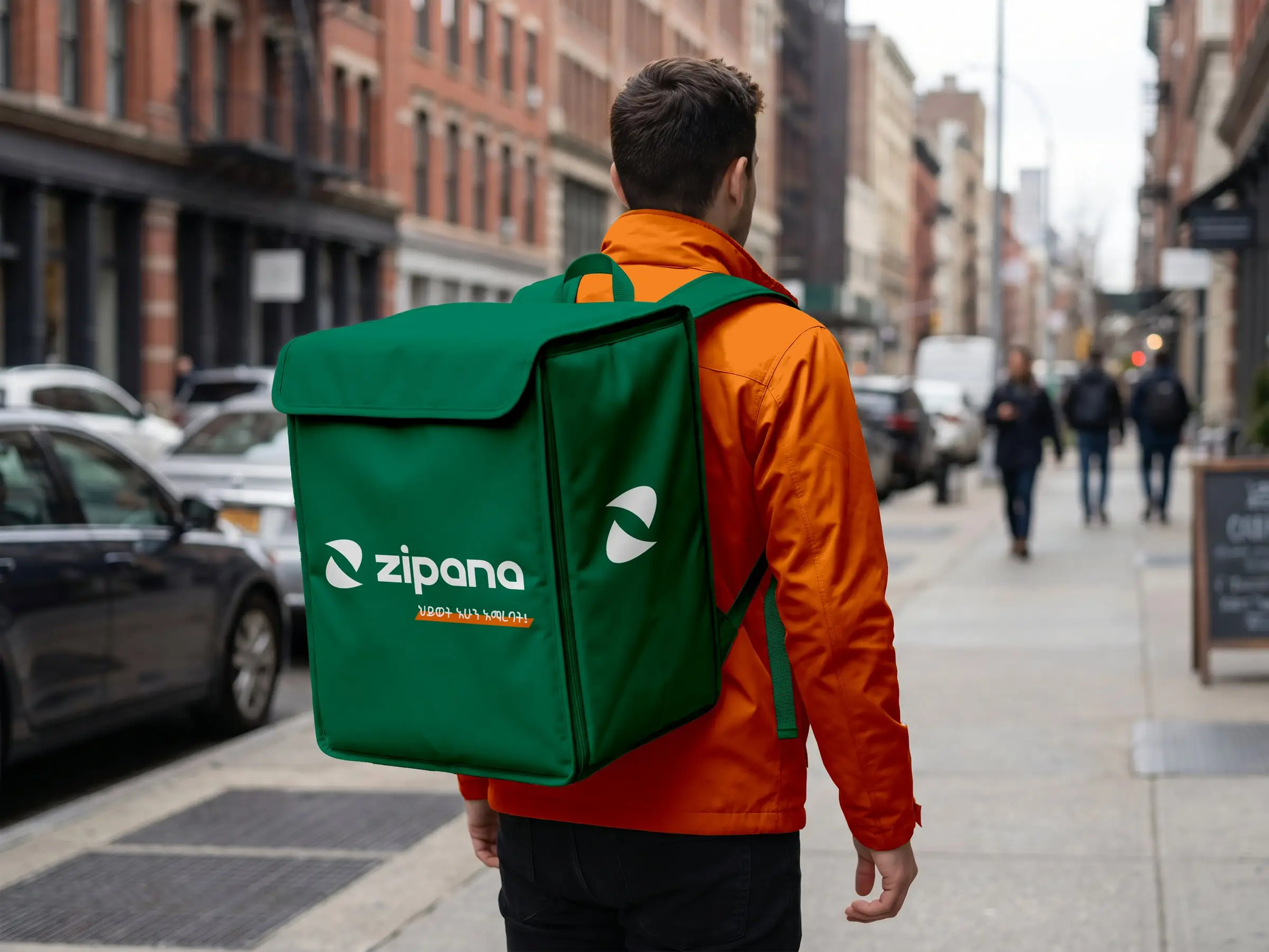 A courier in an orange jacket walks a city street carrying a green delivery backpack