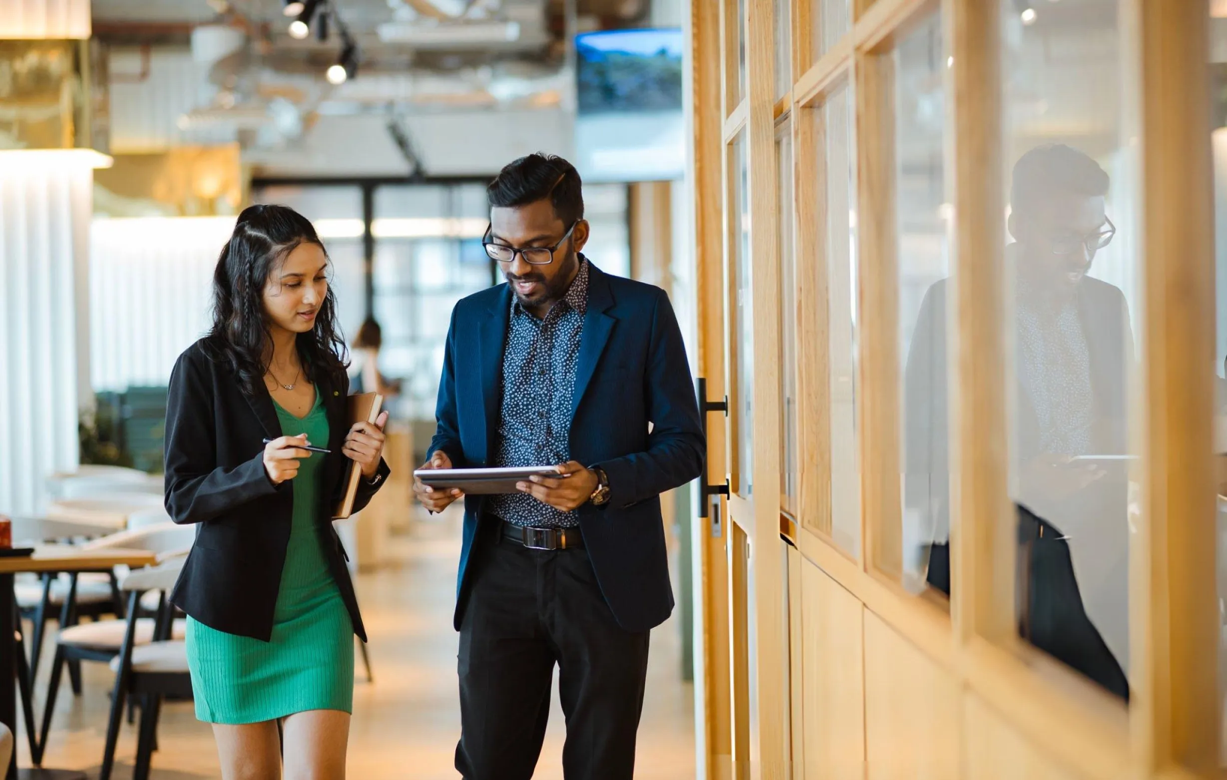 Two colleagues in conversation with a tablet while walking through an office